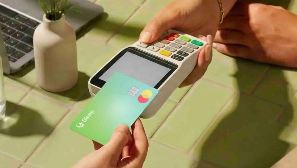 Person making a contactless payment by tapping a green card on a handheld card reader at a checkout counter.